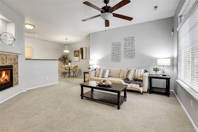 living room featuring a ceiling fan, light carpet, baseboards, and a tile fireplace