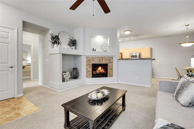 living area with light colored carpet, a ceiling fan, a tiled fireplace, and baseboards