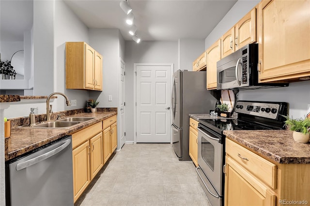 kitchen featuring appliances with stainless steel finishes, a sink, light brown cabinets, and dark countertops