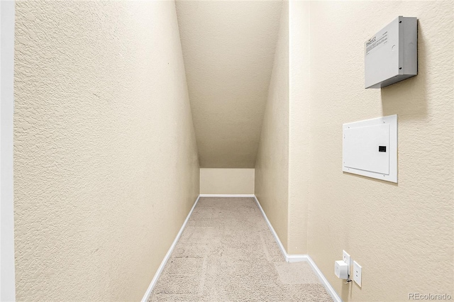 hallway with carpet, baseboards, a textured wall, and lofted ceiling