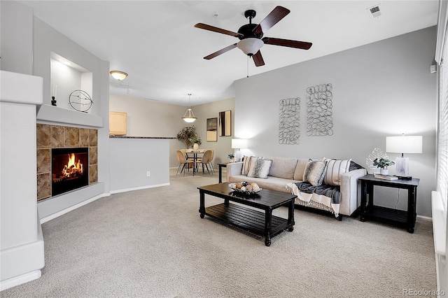 living area with ceiling fan, light carpet, baseboards, and a tiled fireplace