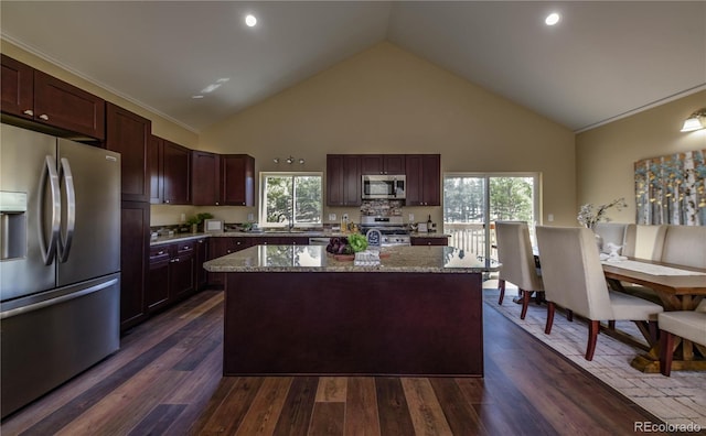 kitchen with appliances with stainless steel finishes, a kitchen island, light stone counters, and dark hardwood / wood-style flooring