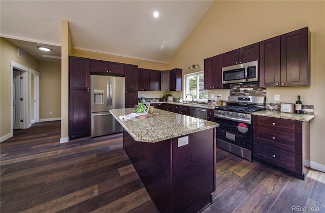 kitchen with dark wood-type flooring, high vaulted ceiling, stainless steel appliances, a center island, and light stone countertops