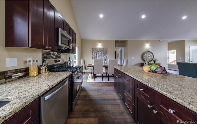 kitchen featuring light stone counters, dark hardwood / wood-style floors, tasteful backsplash, vaulted ceiling, and appliances with stainless steel finishes