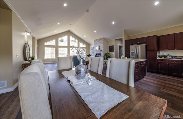 dining room with lofted ceiling, crown molding, a stone fireplace, and dark hardwood / wood-style floors