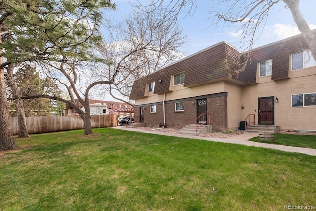 back of property featuring roof with shingles, a lawn, mansard roof, fence, and stucco siding