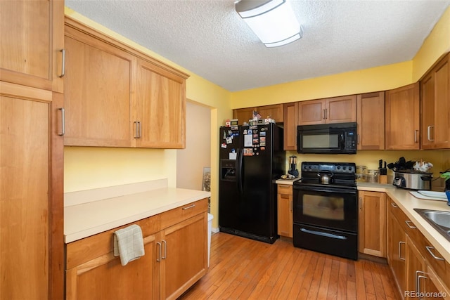kitchen with light wood-style floors, light countertops, a textured ceiling, a sink, and black appliances
