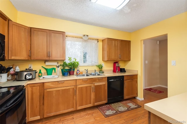 kitchen with a textured ceiling, a sink, light countertops, black appliances, and light wood finished floors
