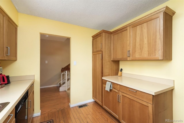kitchen featuring visible vents, dishwasher, light countertops, baseboards, and light wood-style flooring