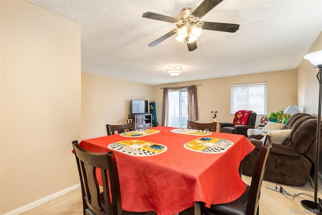 dining area featuring a ceiling fan, a textured ceiling, light colored carpet, and baseboards