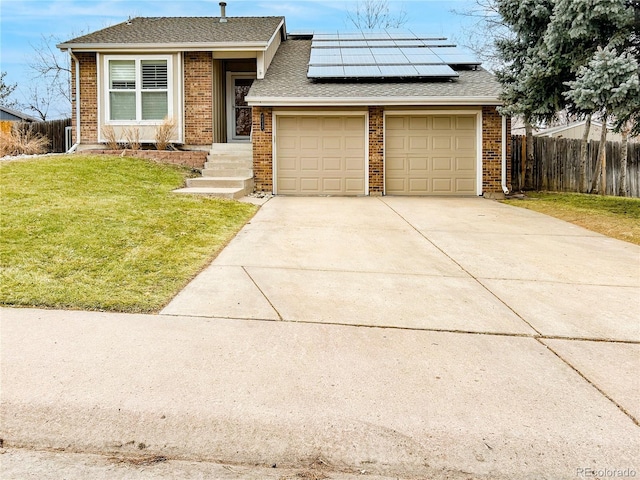 view of front of property featuring driveway, brick siding, fence, and roof mounted solar panels