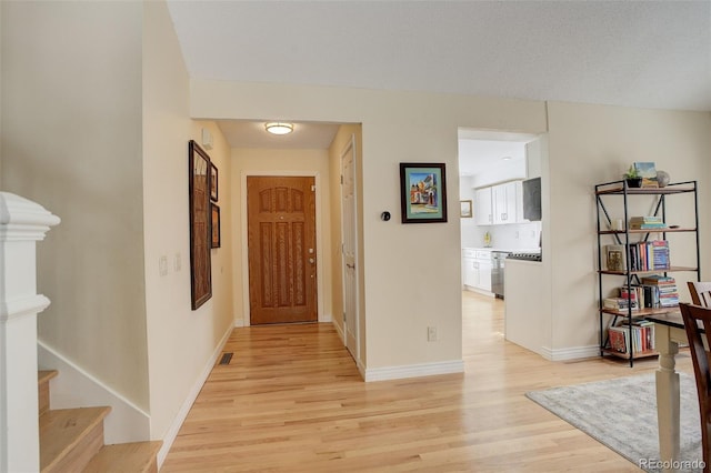 hallway featuring light wood-type flooring, visible vents, stairway, and baseboards