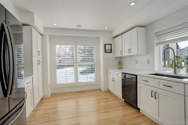 kitchen with a sink, white cabinetry, black dishwasher, light countertops, and stainless steel refrigerator