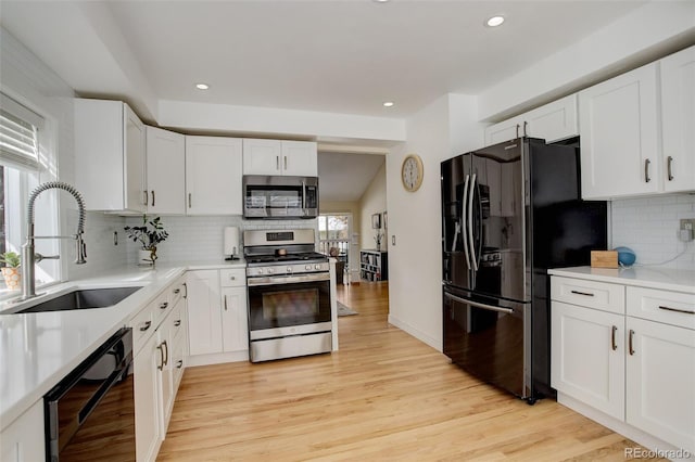 kitchen with light countertops, white cabinetry, a sink, light wood-type flooring, and black appliances