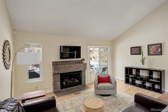 living room featuring vaulted ceiling, light wood finished floors, plenty of natural light, and a fireplace