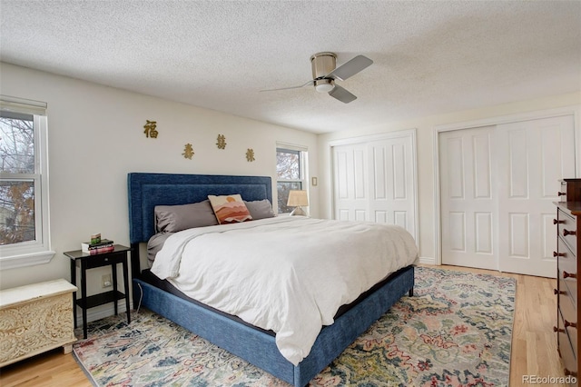 bedroom featuring ceiling fan, a textured ceiling, wood finished floors, and multiple closets