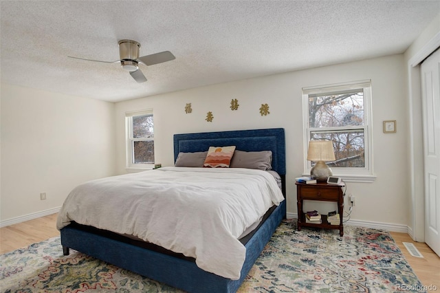 bedroom featuring baseboards, visible vents, a ceiling fan, a textured ceiling, and light wood-style floors