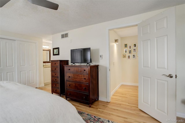 bedroom with a closet, visible vents, light wood-style floors, a textured ceiling, and baseboards