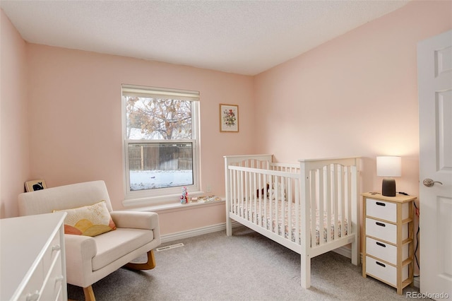 carpeted bedroom with a textured ceiling, a crib, and baseboards