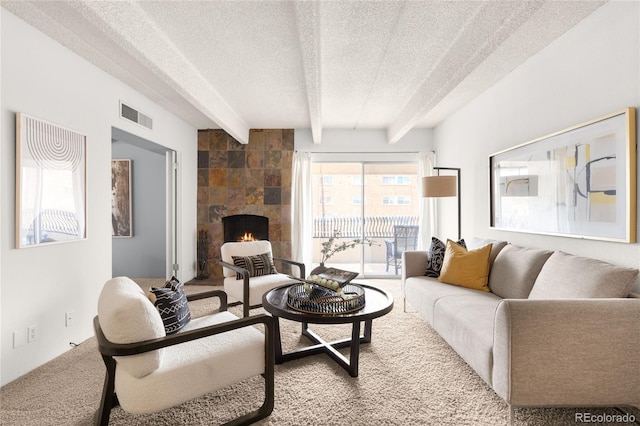 living area featuring visible vents, beam ceiling, a tile fireplace, a textured ceiling, and carpet flooring