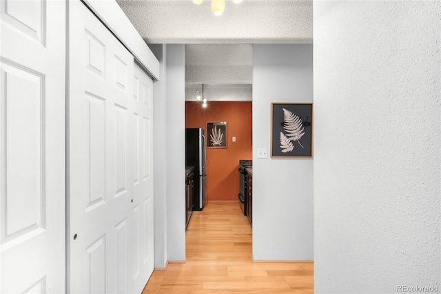 corridor with light wood-type flooring and a textured ceiling