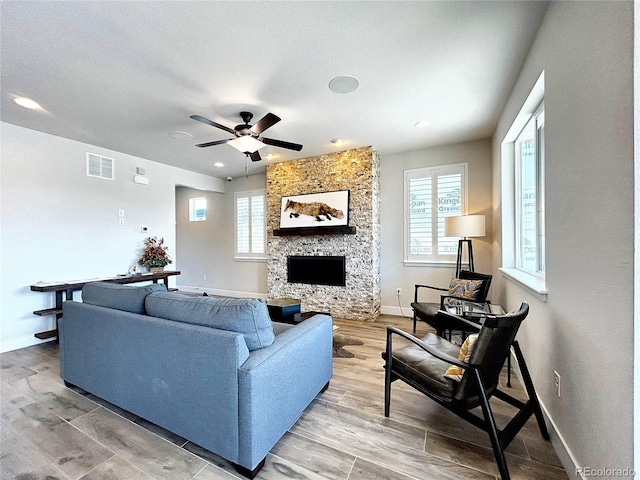 living room featuring ceiling fan, a stone fireplace, and hardwood / wood-style floors