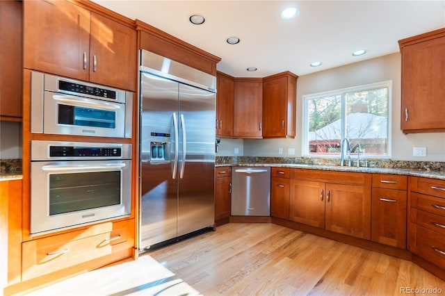 kitchen with light stone counters, sink, stainless steel appliances, and light wood-type flooring