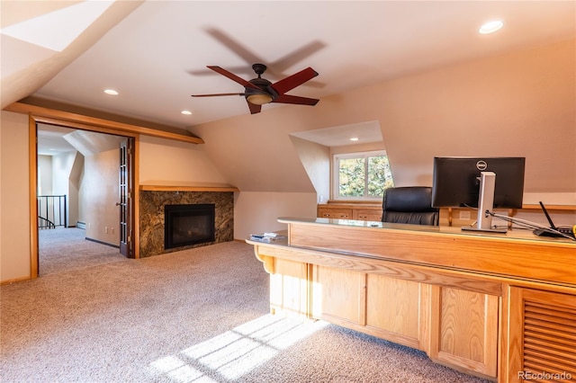 unfurnished office featuring light carpet, a fireplace, lofted ceiling, and ceiling fan