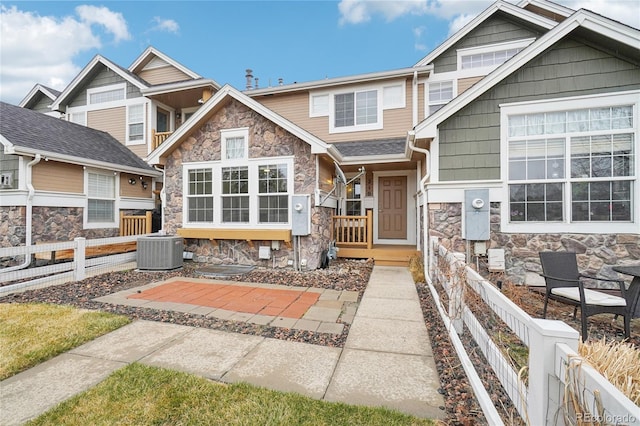 view of front facade with fence, central AC unit, covered porch, and stone siding