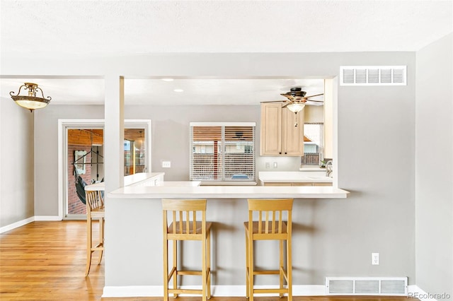 kitchen with light hardwood / wood-style flooring, a kitchen bar, ceiling fan, and light brown cabinets