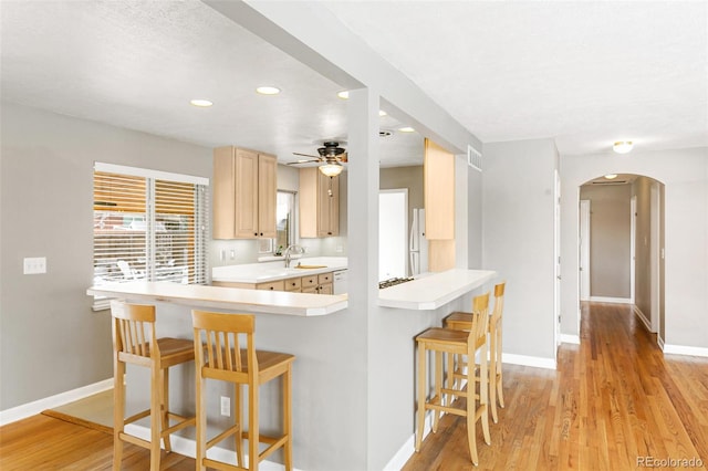 kitchen featuring white fridge, sink, light brown cabinetry, kitchen peninsula, and a breakfast bar area