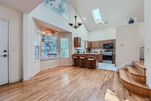 18872 E Prentice Pl, Centennial, CO 80015 - kitchen with stainless steel range with electric cooktop, black microwave, a skylight, high vaulted ceiling, and light wood finished floors