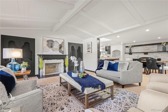 living room with light hardwood / wood-style flooring, lofted ceiling with beams, and a large fireplace