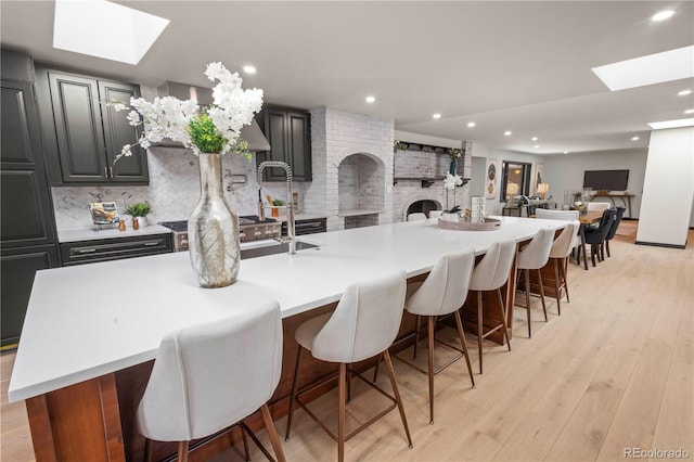 kitchen featuring a large island with sink, decorative backsplash, a kitchen bar, a fireplace, and light hardwood / wood-style floors