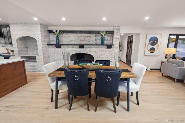 dining room featuring brick wall, light hardwood / wood-style flooring, and a brick fireplace