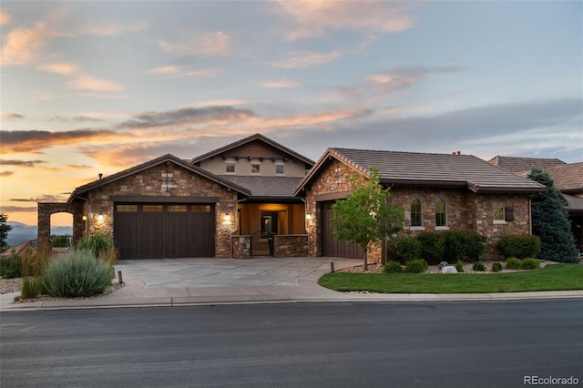 view of front of home with stone siding, driveway, a tiled roof, and an attached garage