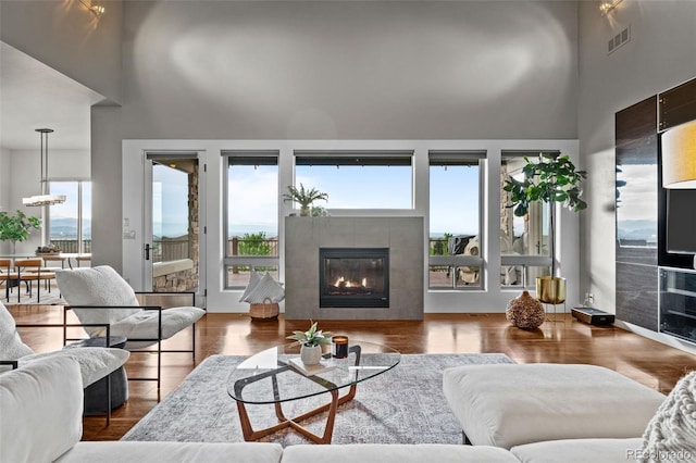 living area featuring visible vents, a tiled fireplace, wood finished floors, a high ceiling, and a notable chandelier