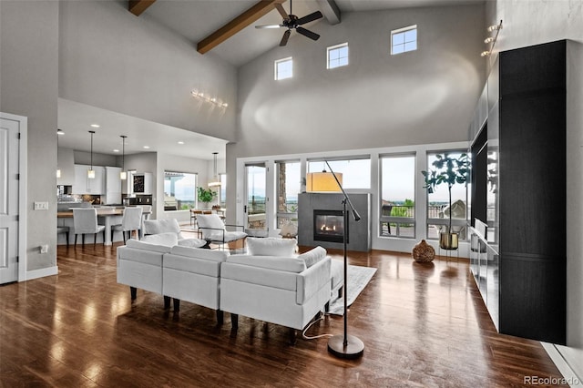 living room with lofted ceiling with beams, dark wood-type flooring, a glass covered fireplace, and a ceiling fan