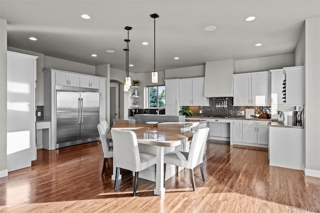 kitchen featuring wood finished floors, built in refrigerator, a kitchen bar, and a kitchen island