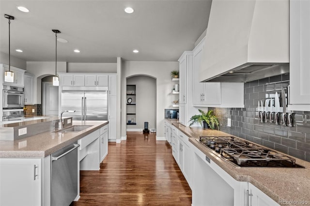 kitchen with arched walkways, stainless steel appliances, dark wood-style flooring, a sink, and custom range hood