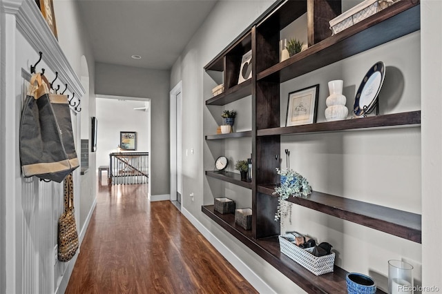 hall featuring dark wood-style flooring, an upstairs landing, and baseboards