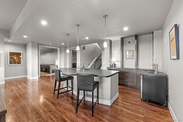 kitchen featuring a kitchen island with sink, recessed lighting, a breakfast bar, dark wood-style flooring, and dark countertops