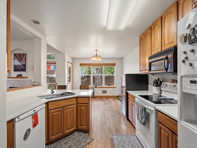kitchen with brown cabinetry, an inviting chandelier, a sink, and white appliances