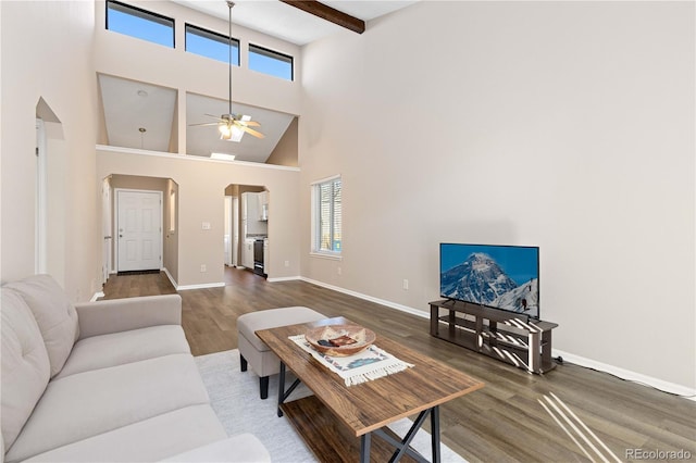 living room with a towering ceiling, arched walkways, wood finished floors, and beamed ceiling