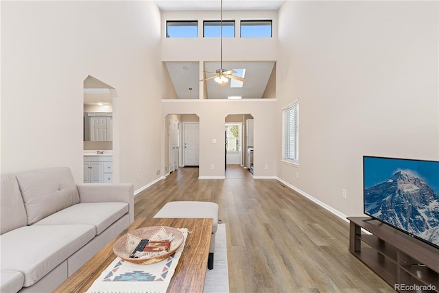 living area with baseboards, a high ceiling, arched walkways, and wood finished floors