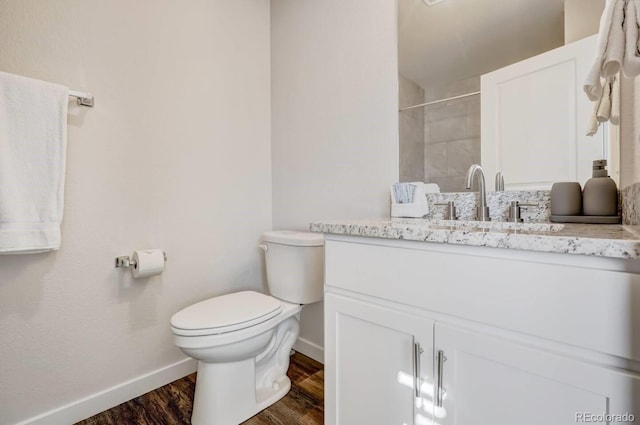 bathroom with tiled shower, toilet, baseboards, wood finished floors, and vanity