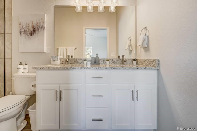 full bathroom featuring double vanity, toilet, a textured wall, and a sink