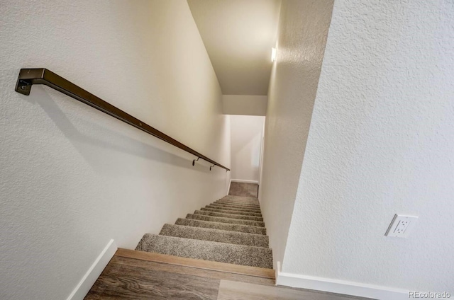 stairway featuring a textured wall, wood finished floors, and baseboards