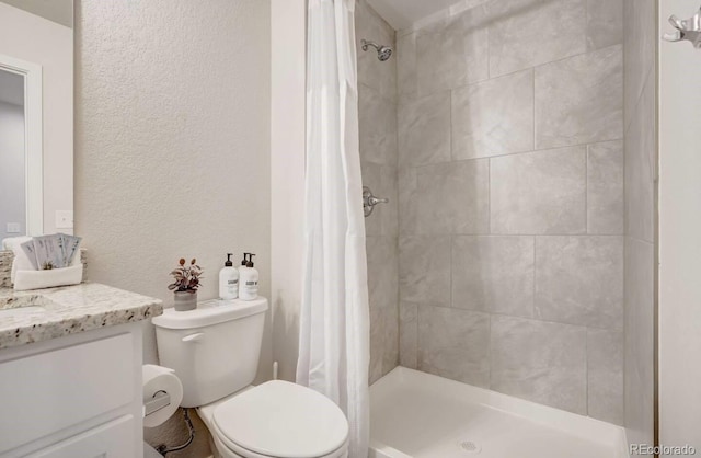 full bath featuring a textured wall, vanity, a shower stall, and toilet