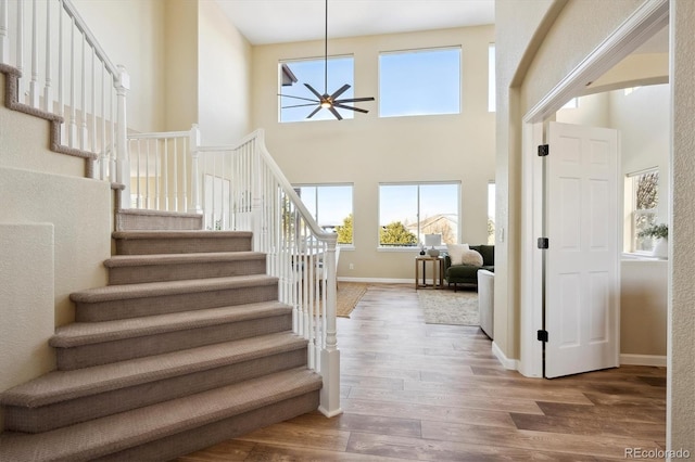 staircase with a towering ceiling, wood-type flooring, and ceiling fan